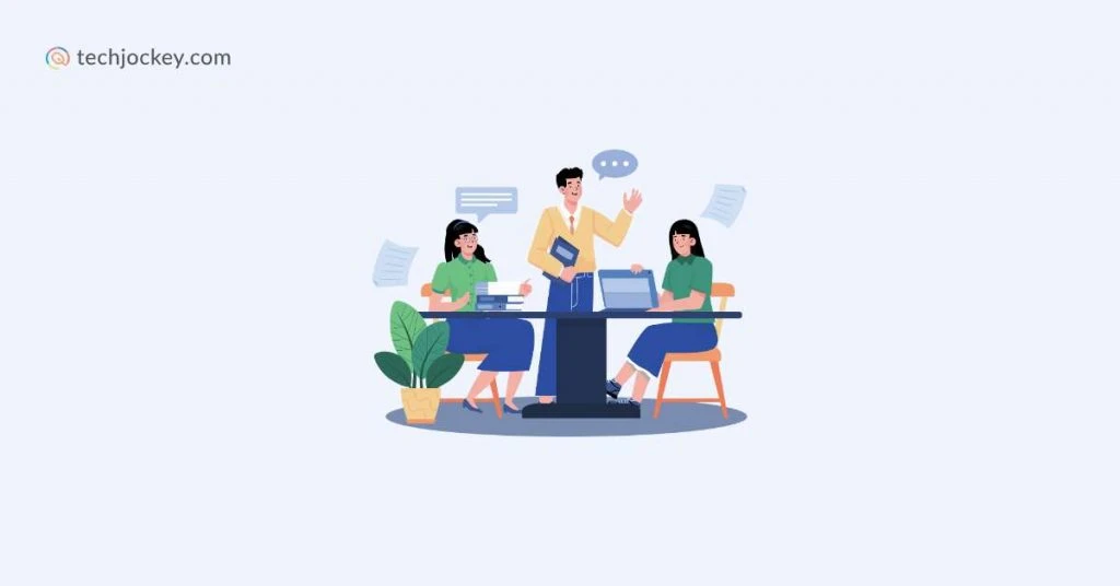 Business meeting with three people discussing projects at a table with laptops books and speech bubbles