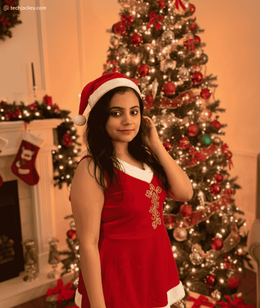 Woman in a maroon dress decorating a Christmas tree with lights and ornaments in a warmly lit festive living room