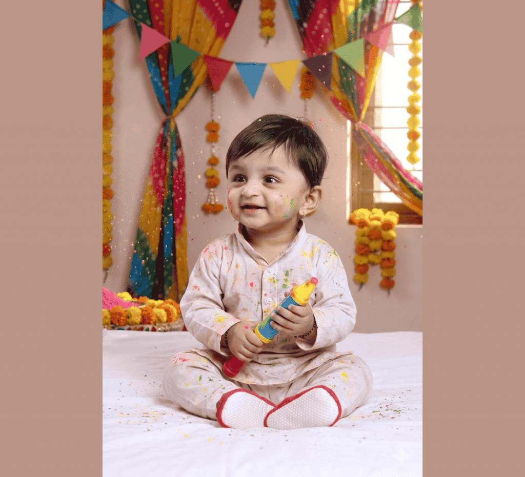 Toddler holding pichkari wearing traditional outfit with Holi decorations and marigold garlands in background.
